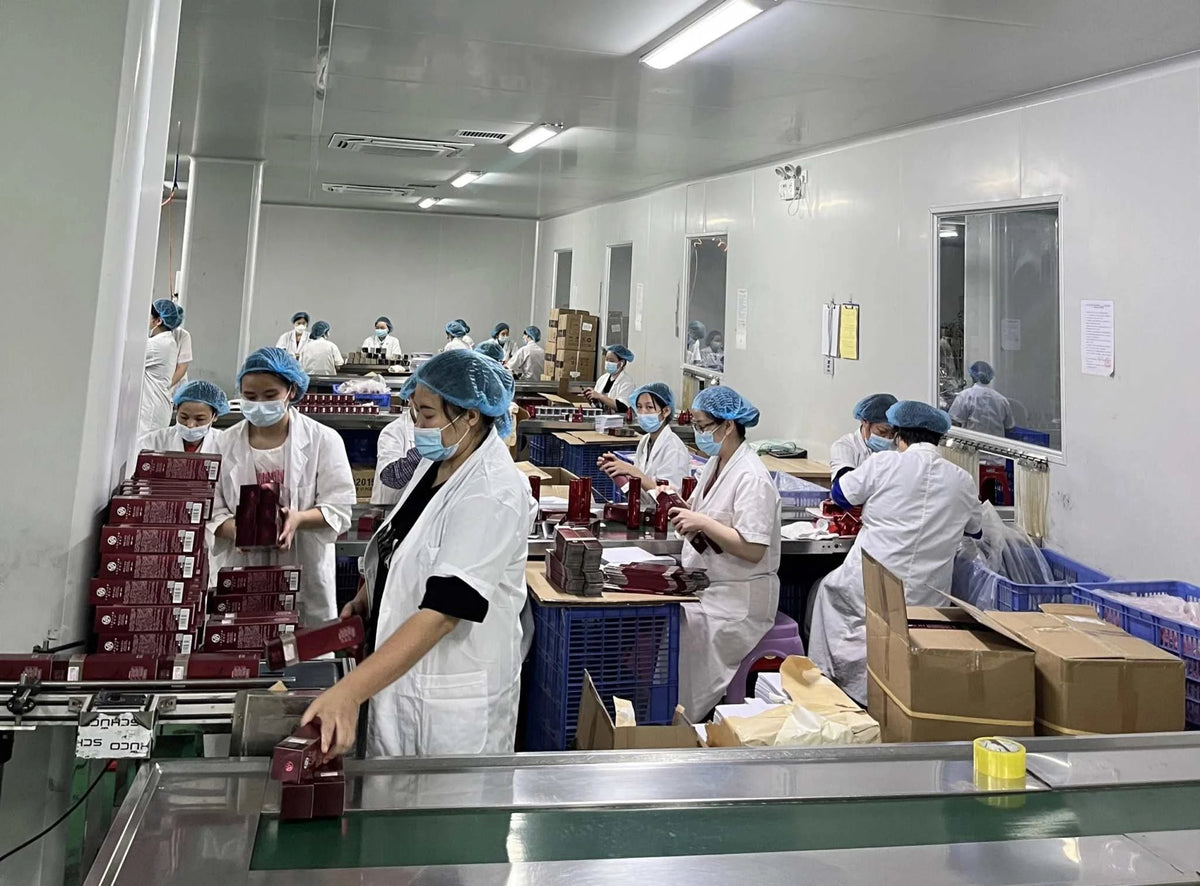 Anti-aging Retinol face cream being packaged in red boxes by workers wearing white coats and blue hairnets