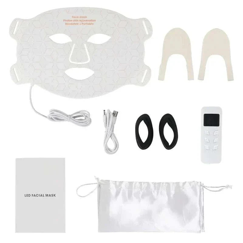 Home Use Therapy Face Device consisting of a white flexible silicone LED facial mask with geometric pattern, control remote, cables, black eye pads, beige nose grips, instruction booklet, and white drawstring pouch